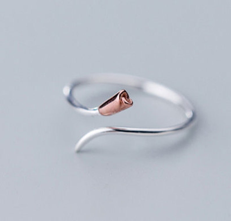 May include: A silver ring with a rose gold swirl design. The ring has a delicate, feminine look.