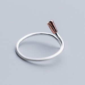 May include: A silver ring with a rose gold flower detail. The ring is simple and elegant.