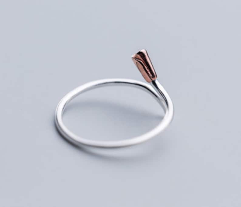 May include: A silver ring with a rose gold flower detail. The ring is simple and elegant.