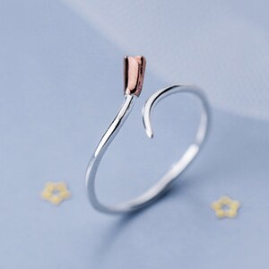 May include: A silver ring with a rose gold accent on the top. The ring is shaped like a curved line.