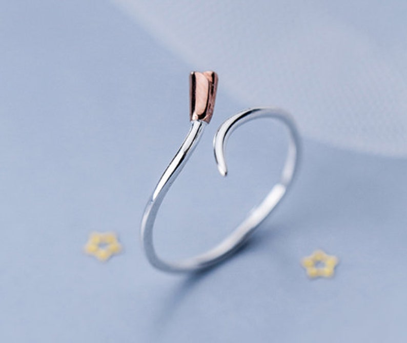 May include: A silver ring with a rose gold accent on the top. The ring is shaped like a curved line.