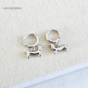 Könnte beinhalten: Ein Paar silberne Creolen mit einem silbernen Dackel-Anhänger, der an jeder Creole hängt.