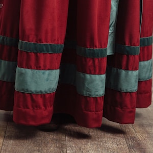 Op de afbeelding: Close-up van een rode fluwelen rok met horizontale banden in zeegroen. De rok maakt deel uit van een kostuum, met de winkelnaam "A l'Entrada SHOP" zichtbaar linksboven. De rok hangt, met de zoom zichtbaar.