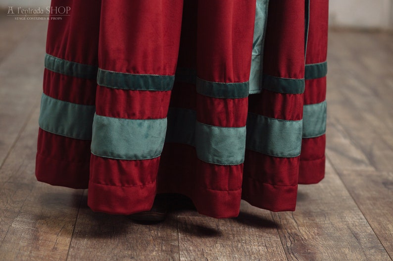 Op de afbeelding: Close-up van een rode fluwelen rok met horizontale banden in zeegroen. De rok maakt deel uit van een kostuum, met de winkelnaam "A l'Entrada SHOP" zichtbaar linksboven. De rok hangt, met de zoom zichtbaar.