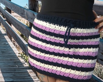 May include: A striped crochet skirt with a drawstring waist. The skirt is made with white, purple, and black yarn.