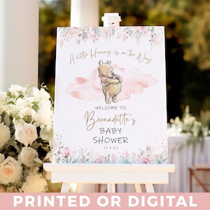 May include: A Winnie the Pooh themed baby shower welcome sign with pink and green floral accents. The sign features a watercolour background with the text "A little Hunny is on the Way" and "Welcome to Bernadette's Baby Shower 11.5.23".