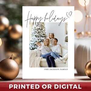 May include: A white holiday card with a family photo, a Christmas tree, and the text "Happy holidays" in cursive. The card also includes the text "-THE JACKSON FAMILY" and the words "PRINTED OR DIGITAL" in a red banner.