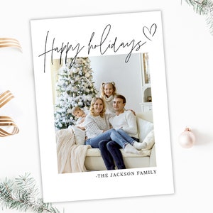 May include: A white holiday card with the words "Happy holidays" in elegant script, a heart symbol, and a family photo. The family is seated in front of a Christmas tree. The text "- THE JACKSON FAMILY" is at the bottom.
