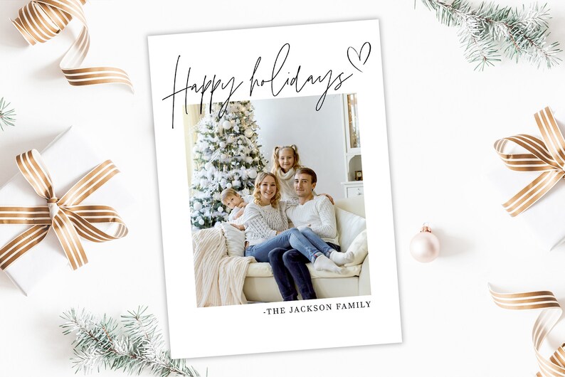 May include: A white holiday card with the words "Happy holidays" in elegant script, a heart symbol, and a family photo. The family is seated in front of a Christmas tree. The text "- THE JACKSON FAMILY" is at the bottom.