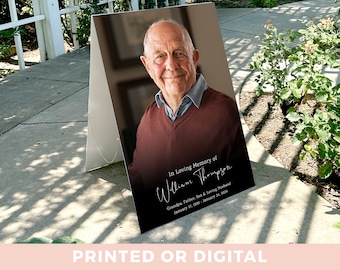 May include: A black and white memorial sign with a photo of a man and the text "In Loving Memory of William Thompson Grandpa, Father, Son & Loving Husband January 17, 1939 - January 24, 2014".