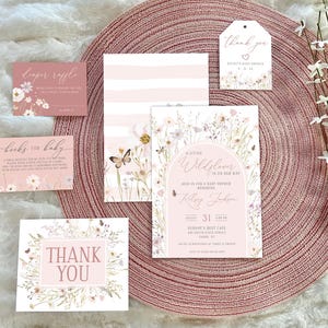May include: A set of baby shower stationery including an invitation, diaper raffle card, books for baby card, and thank you tags. The cards feature a soft pink and white color palette with watercolor wildflower illustrations, butterflies, and elegant script text.