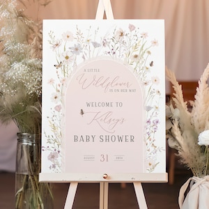 May include: A rectangular baby shower welcome sign featuring a soft pink arch design, watercolor wildflowers, and butterflies. The text reads: A LITTLE Wildflower IS ON HER WAY, WELCOME TO Kelsey's BABY SHOWER, AUGUST 31 2024. The sign is on an easel.