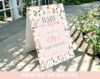 May include: A pink and white baby shower sign with floral designs. The sign reads "Baby in Bloom" and "Welcome to Kaly's Baby Shower".