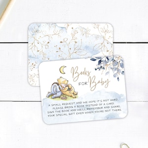 May include: Two rectangular baby shower cards. The top card has a watercolor floral design in gold and blue. The bottom card features Winnie the Pooh and Eeyore, with text that reads "Books for Baby". The card requests a book instead of a card.