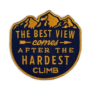 Peut inclure: Un écusson brodé bleu marine avec un motif de chaîne de montagnes et le texte "The best view comes after the hardest climb" en fil doré.