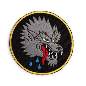 May include: A round black and gold embroidered patch with a gray wolf's head with a red tongue and blue dripping saliva. The wolf has a fierce expression with sharp teeth and yellow eyes.