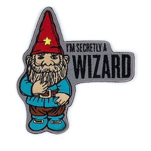 May include: Iron-on patch featuring an embroidered cartoon gnome with a red hat and a grey beard. The gnome is holding a finger to his lips and the text "I'm secretly a wizard" is on a grey background.
