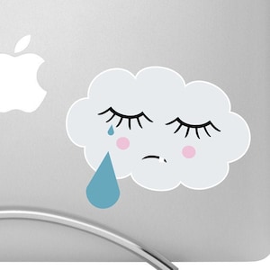 May include: A white cloud with a sad face and a single blue teardrop. The cloud has closed eyes and pink cheeks. The cloud is on a silver laptop with a white apple logo.