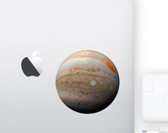 May include: A close-up of a sticker of Jupiter, the largest planet in our solar system, on a silver laptop. The sticker is a realistic depiction of the planet, showing its swirling clouds and the Great Red Spot.