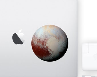 May include: A white laptop with a silver apple logo and a sticker of Pluto, a dwarf planet with a reddish-brown surface and a light blue and white icy cap.