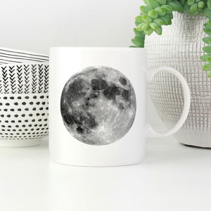 May include: White ceramic mug with a black and white image of the full moon.