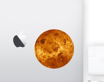 May include: A close-up of a sticker featuring a detailed image of the planet Venus, with a fiery orange and yellow color scheme. The sticker is placed on a silver laptop.