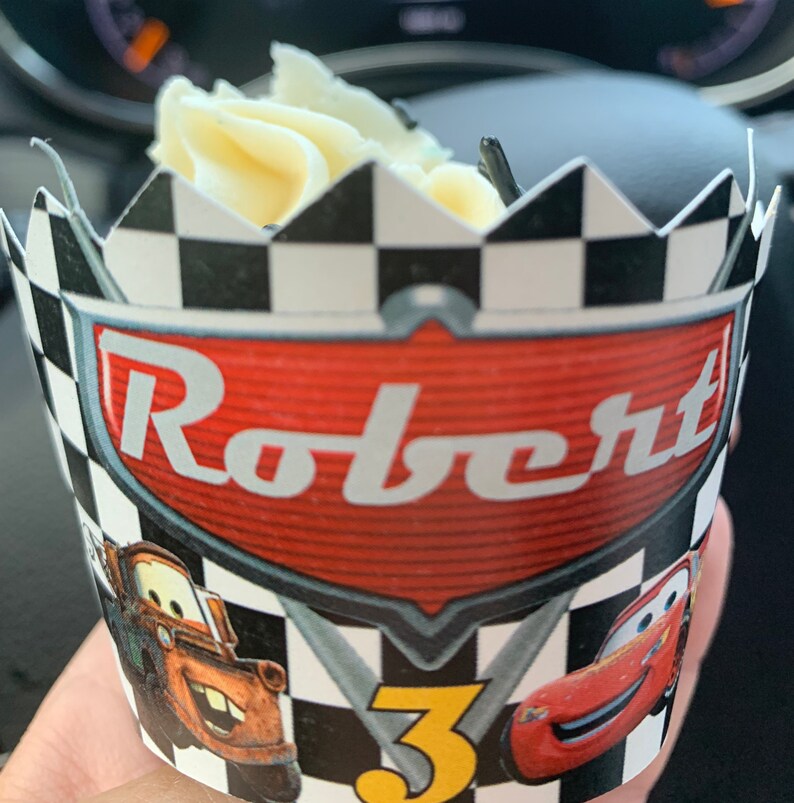 May include: A black and white checkered cupcake wrapper with a red, white, and black Cars themed design. The wrapper features the text "Robert" and the number "3".