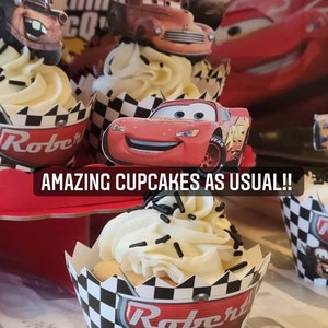 May include: A close-up of cupcakes decorated with Cars characters. The cupcakes are topped with white frosting and black sprinkles. The cupcake wrappers are black and white checkered with the name "Robert" and the number "3" printed on them. The text "AMAZING CUPCAKES AS USUAL!!" is printed on a red background.