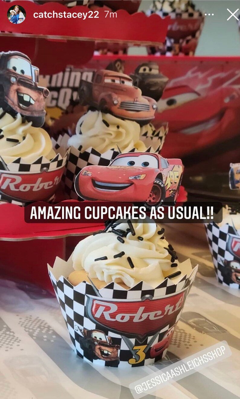 May include: A close-up of cupcakes decorated with Cars characters. The cupcakes are topped with white frosting and black sprinkles. The cupcake wrappers are black and white checkered with the name "Robert" and the number "3" printed on them. The text "AMAZING CUPCAKES AS USUAL!!" is printed on a red background.