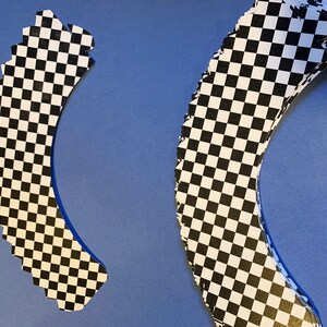May include: Two black and white checkered cupcake wrappers. The wrappers are shaped like a half-circle and have a scalloped edge.