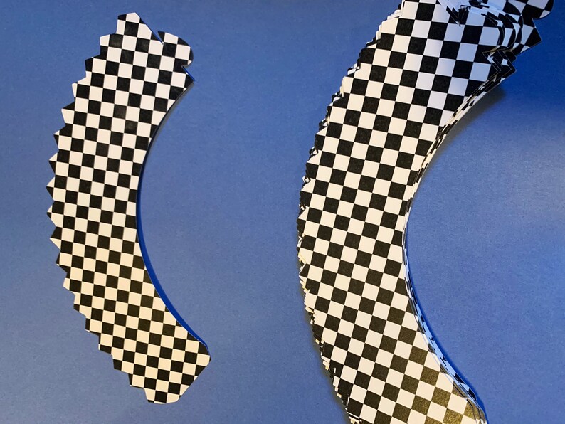 May include: Two black and white checkered cupcake wrappers. The wrappers are shaped like a half-circle and have a scalloped edge.