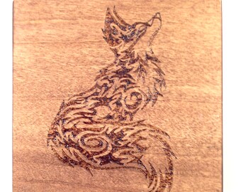 May include: A wooden coaster with a detailed, intricate design of a fox burned into the surface. The fox is facing to the right and has its head tilted up.