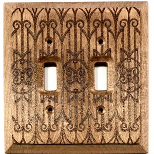 May include: A wooden double light switch cover with an intricate engraved design. The design features a repeating pattern of vertical lines and swirls.