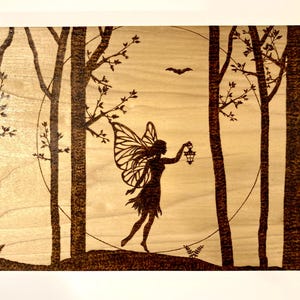 May include: A woodburned image of a fairy with wings holding a lantern in a forest setting with a full moon in the background.
