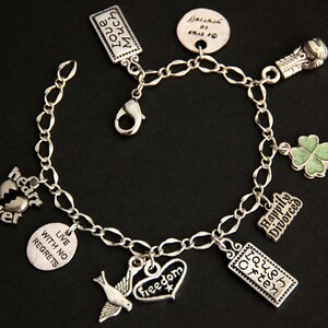 May include: A silver charm bracelet with various charms, including a heart with the words "heart breaker", a clover, a dove, a heart with the word "freedom", a rectangle with the words "laugh often", a rectangle with the words "live with no regrets", a rectangle with the words "happily divorced", and a boxing glove.