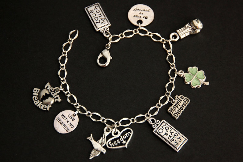 May include: A silver charm bracelet with various charms, including a heart with the words "heart breaker", a clover, a dove, a heart with the word "freedom", a rectangle with the words "laugh often", a rectangle with the words "live with no regrets", a rectangle with the words "happily divorced", and a boxing glove.