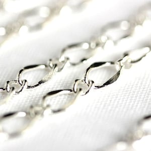 Puede incluir: Primer plano de una cadena de plata con eslabones ovalados. La cadena está sobre una superficie blanca.