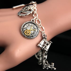 May include: A silver charm bracelet with a variety of charms, including a clock face, gears, and binoculars. The bracelet is on a person's wrist.