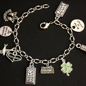 May include: A silver charm bracelet with multiple charms, including a heart with the word "freedom" on it, a dove, a four-leaf clover, a boxing glove, and several rectangular charms with phrases like "Live with no regrets", "Laugh often", "Happily Divorced", "Love much", and "Be true to yourself".