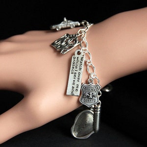 May include: Silver charm bracelet with various police-themed charms, including a police car, badge, fingerprint, and a charm with the text "Watch over me while I serve and protect."