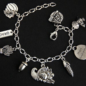 May include: Silver charm bracelet with Thanksgiving themed charms, including a cornucopia, pumpkin, acorn, corn, wheat, turkey, pie, and a tag that says "Happy Thanksgiving".