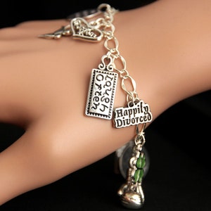 May include: Silver charm bracelet with multiple charms, including a heart charm with the word "Love" on it, a charm with the words "Laugh Often", a charm with the words "Happily Divorced", and a green shamrock charm.