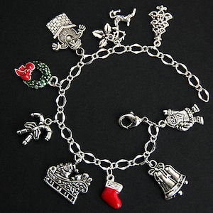 May include: A silver charm bracelet with a variety of Christmas-themed charms, including a snowman, a stocking, a sleigh, a wreath, a candy cane, a bell, a house, a star, and a reindeer.