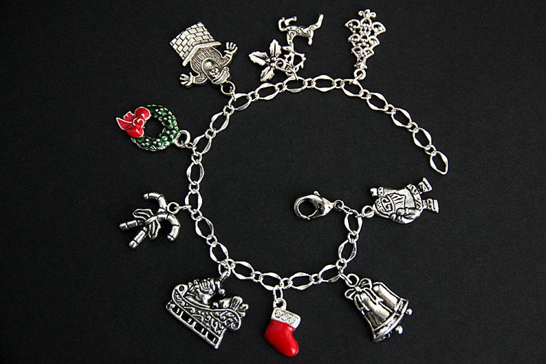 May include: A silver charm bracelet with a variety of Christmas-themed charms, including a snowman, a stocking, a sleigh, a wreath, a candy cane, a bell, a house, a star, and a reindeer.