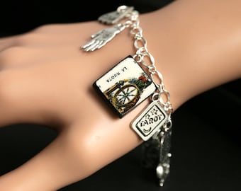 Può includere: Un braccialetto con ciondoli in argento con un ciondolo di carta dei tarocchi che presenta la carta della Ruota della Fortuna, "LA RUOTA", e un ciondolo in argento con la parola "TAROT".