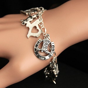 Op de afbeelding: Zilveren armband met meerdere bedels, waaronder een hoefijzer, een laars, een hart en een staatsgrens.