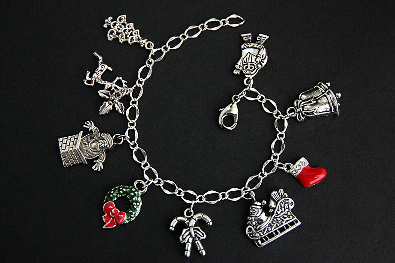 May include: A silver charm bracelet with Christmas-themed charms, including a snowman, a stocking, a wreath, a candy cane, a bell, a reindeer, and a Santa Claus in a sleigh.