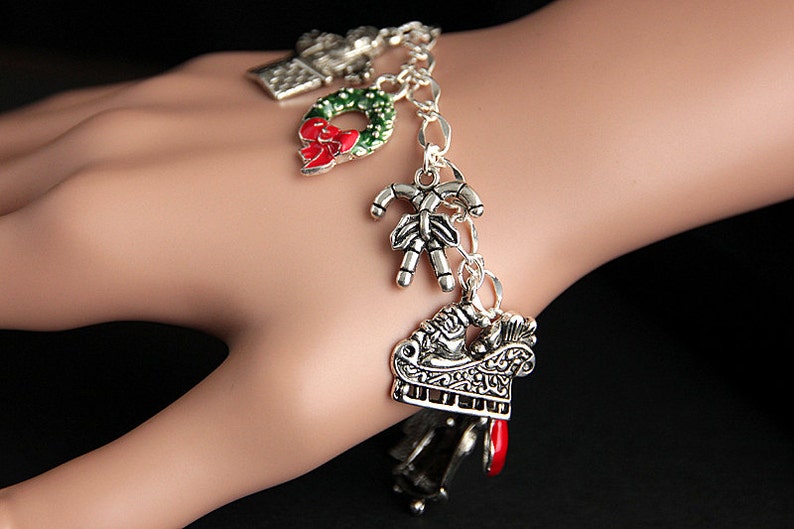 May include: Silver charm bracelet with Christmas themed charms, including a wreath, candy cane, and a sleigh.