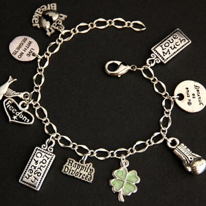 May include: A silver charm bracelet with multiple charms, including a heart with the word "Freedom" on it, a bird, a four-leaf clover, a boxing glove, and several rectangular charms with text. The text on the charms includes "Live with no regrets", "Hear Breaker", "Laugh Often", "Love Much", "Happily Divorced", and "Be true to yourself".
