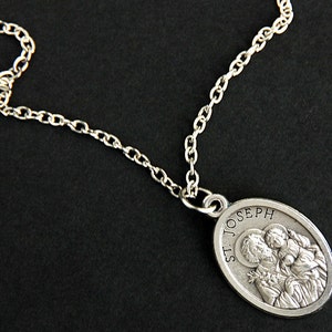 Peut inclure: Un collier en cha&icirc;ne argent&eacute;e avec un pendentif ovale repr&eacute;sentant une image en relief de Saint Joseph tenant l'enfant J&eacute;sus. Le pendentif est inscrit "St. Joseph".